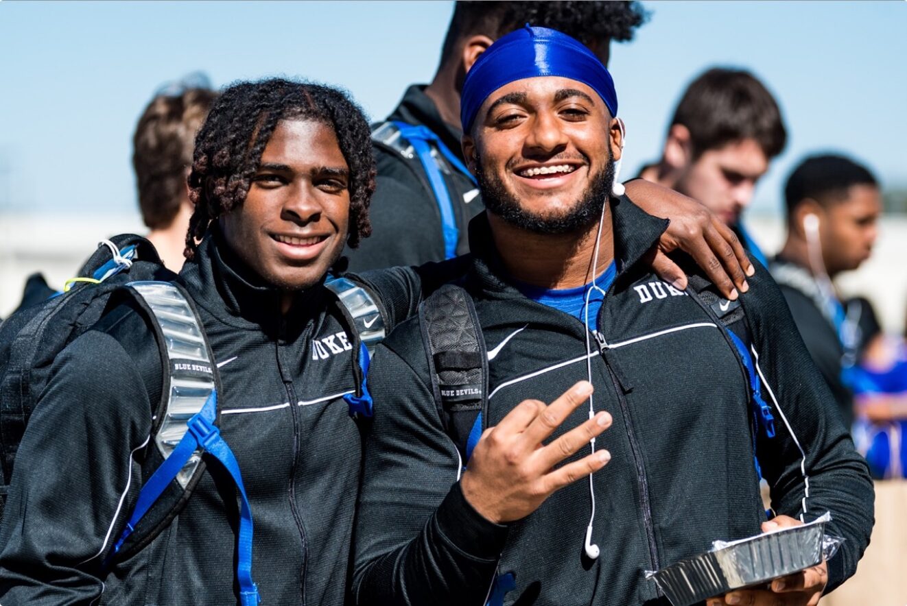 Two Duke Blue Devils football players in casual attire, smiling and posing for the camera.