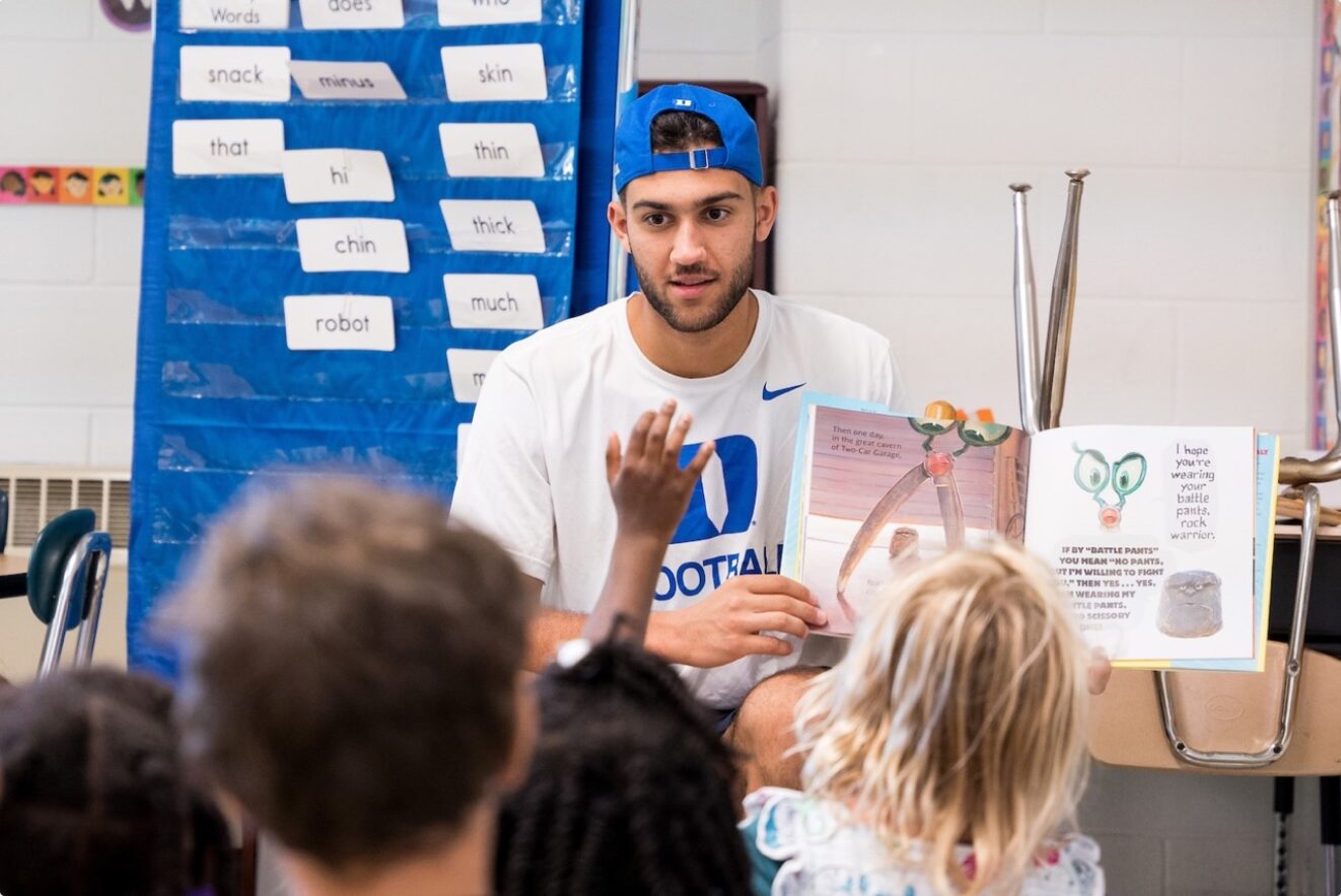 Duke Football player reading a book to a group of children